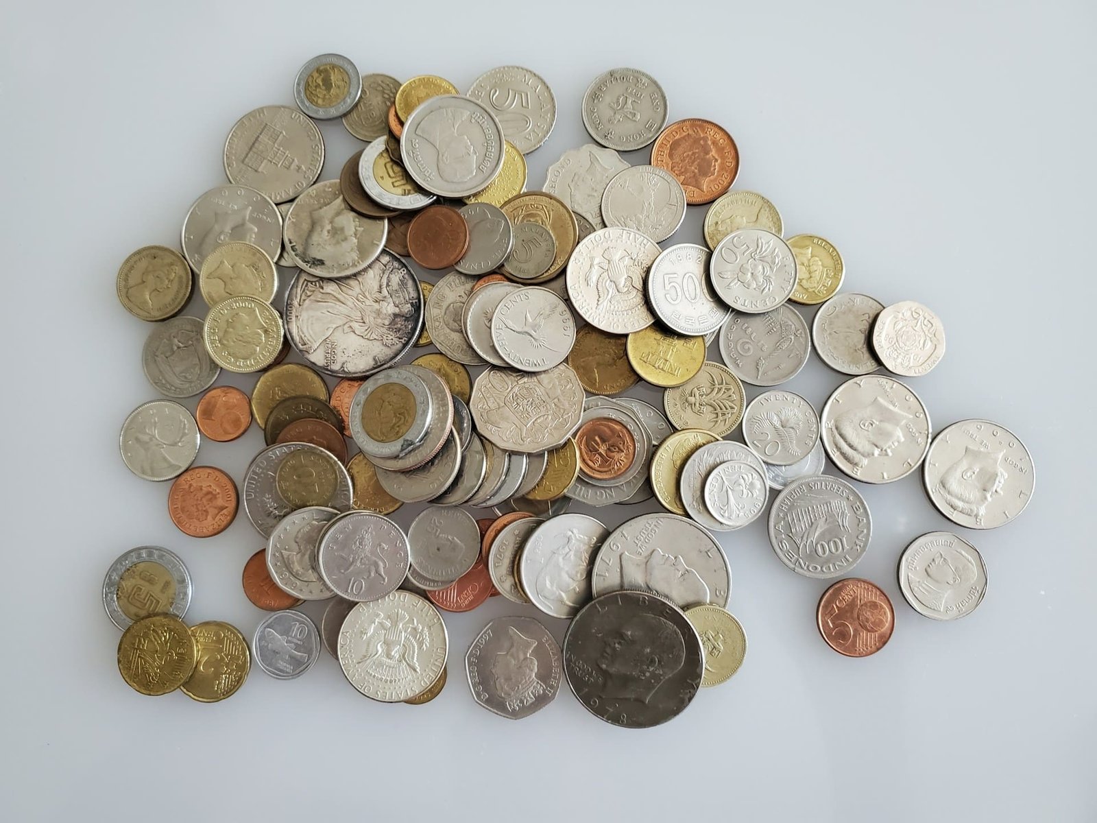 A scattered collection of international coins on a white background, symbolizing the complexity of global payments and financial policy. Photo by Kevin Dunlap on Unsplash.